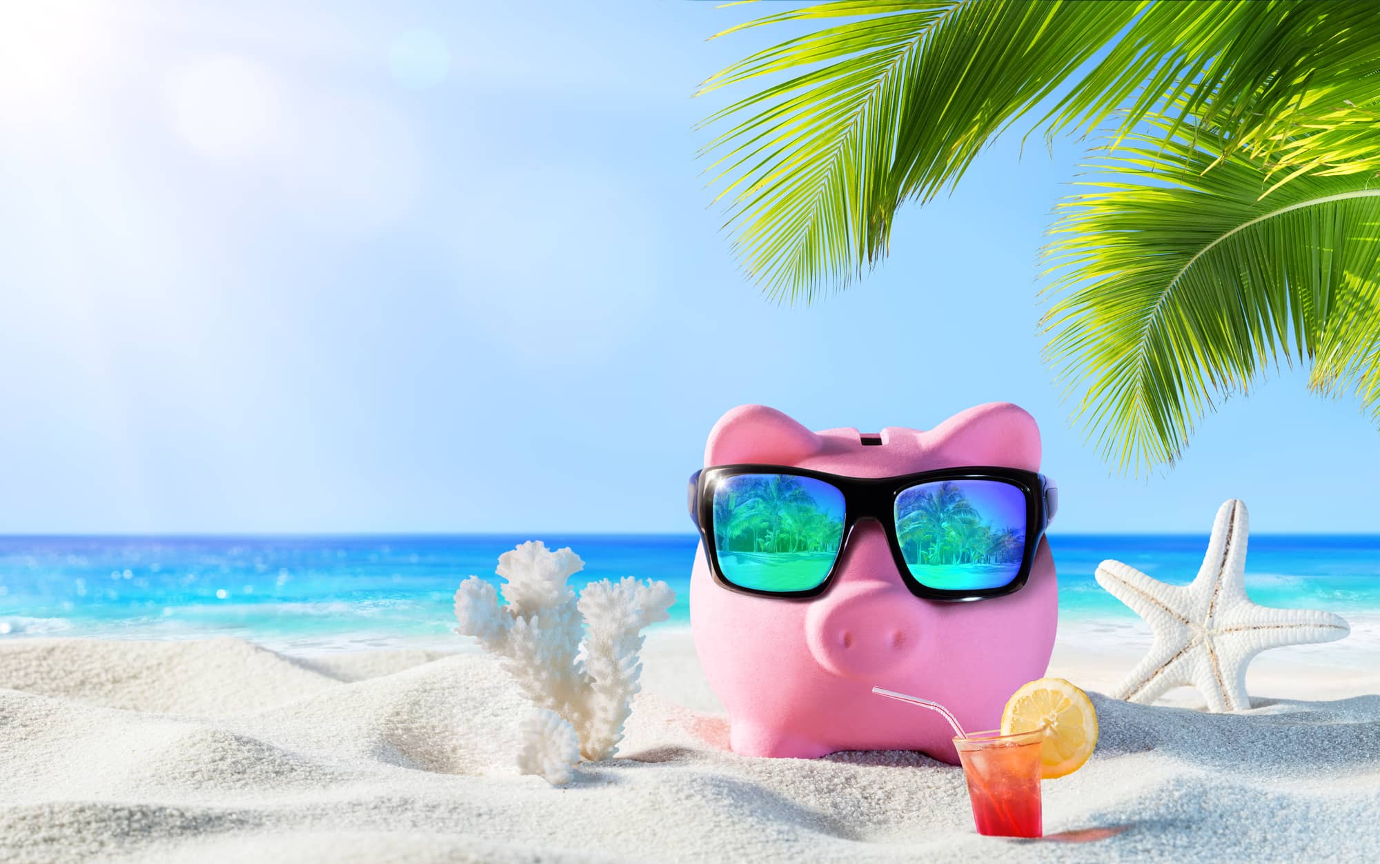 Piggy bank wearing sunglasses and hanging out on the beach with a cold drink.