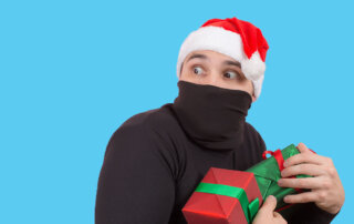 Man dressed in black wearing a santa hat while stealing gifts..