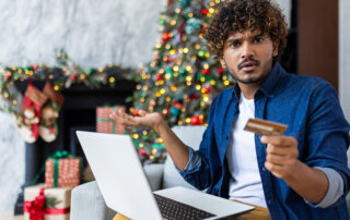 Confused man with laptop holding a credit card.